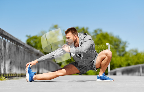 Image of man stretching leg on bridge