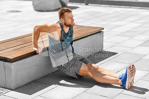 Image of young man doing triceps dip on city street