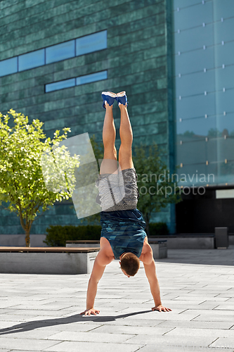 Image of young man exercising and doing handstand outdoors