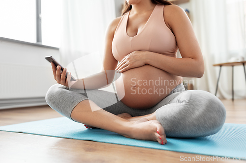 Image of happy pregnant woman with phone doing yoga at home