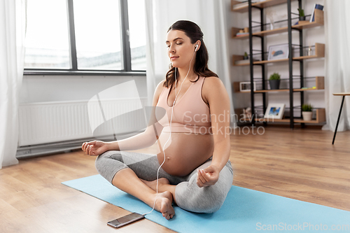 Image of pregnant woman with earphones doing yoga at home