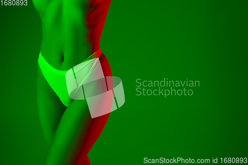 Image of Beautiful female belly on green background in neon light. Beauty, cosmetics, spa, depilation, diet and treatment, fitness concept.