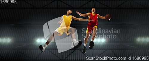 Image of Young basketball players in competitive fight, motion in flight on black background, look from the bottom. Concept of sport, movement, energy and dynamic.