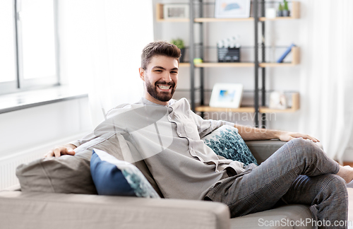 Image of happy smiling man sitting on sofa at home