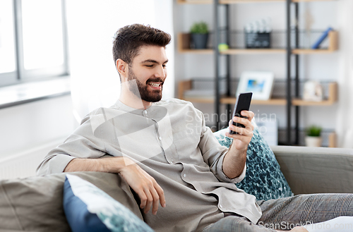 Image of happy smiling young man with smartphone at home
