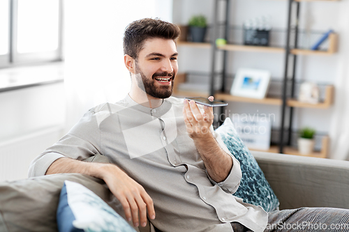 Image of happy man with smartphone recording voice at home