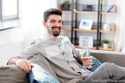 Image of happy man drinking water from glass bottle at home