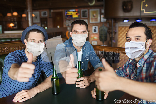 Image of male friends in masks drinking beer at bar or pub