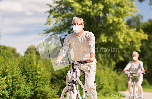 Image of senior couple in masks riding bicycles at park