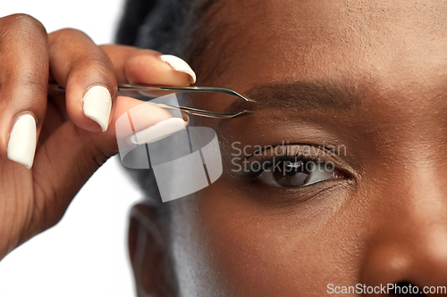 Image of african woman with tweezers tweezing her eyebrow