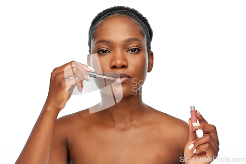 Image of african american woman applying lip gloss