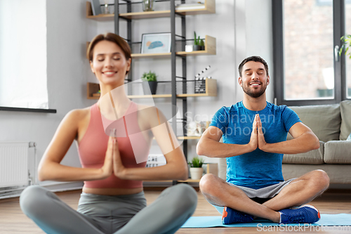 Image of happy couple meditating in yoga lotus pose at home