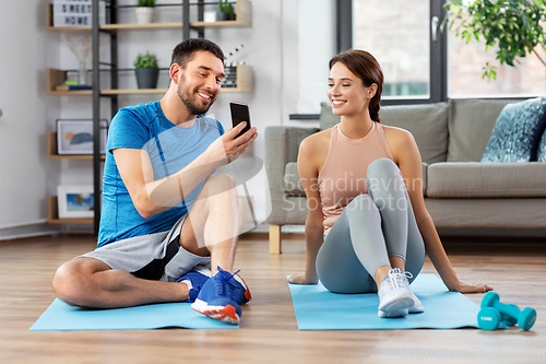 Image of happy couple with smartphone doing sports at home