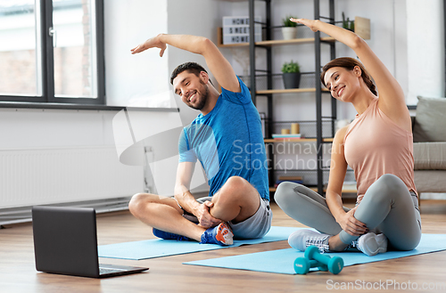 Image of happy couple with laptop exercising at home