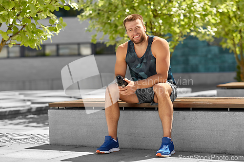 Image of happy sportsman with bottle sitting on city bench