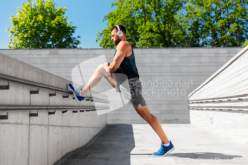 Image of young man in headphones stretching leg outdoors