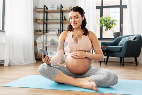 Image of happy pregnant woman sitting on yoga mat at home