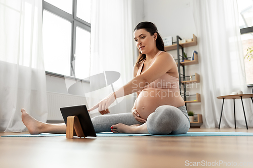 Image of pregnant woman with tablet pc doing sports at home