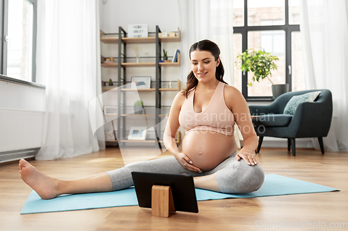 Image of pregnant woman with tablet pc doing sports at home