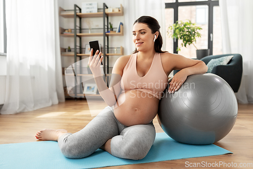 Image of pregnant woman with smartphone and fitball at home