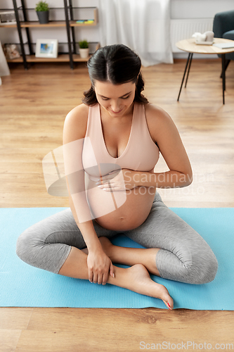 Image of happy pregnant woman sitting on yoga mat at home