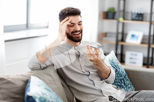 Image of happy man with smartphone recording voice at home