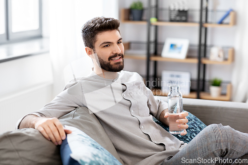 Image of happy man drinking water from glass bottle at home