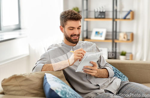 Image of smiling man writing to notebook at home