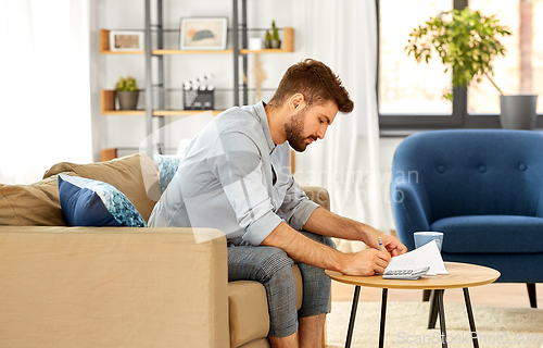 Image of man with bills counting on calculator at home