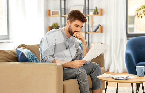 Image of man with bills counting on calculator at home