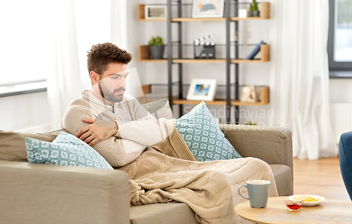 Image of sick young man in blanket with hot tea at home