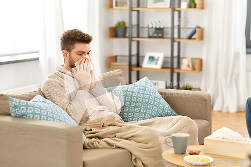 Image of sick man blowing nose in paper tissue at home