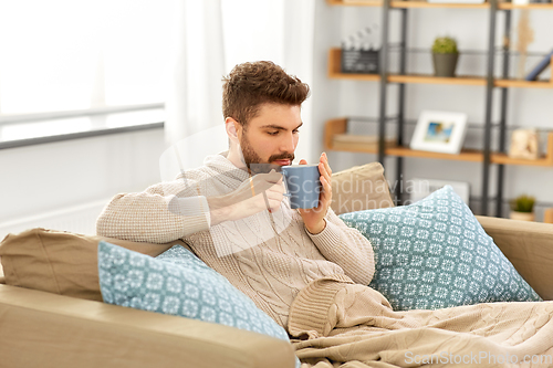 Image of sick young man in blanket drinking hot tea at home