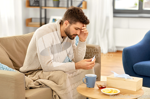 Image of sick man measuring temperature by thermometer