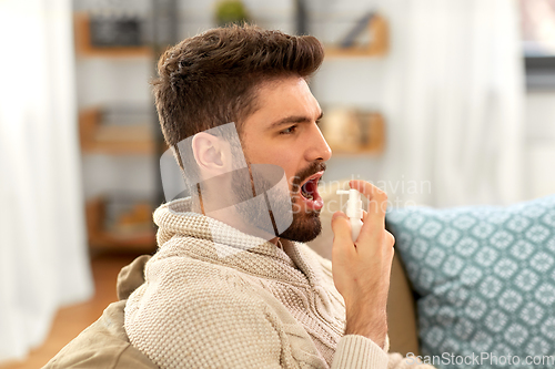 Image of sick indian man using oral spray at home