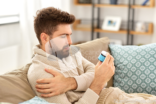 Image of sad sick man in blanket with medicine at home