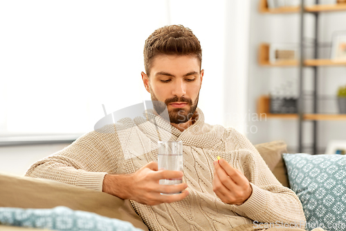 Image of sick man with glass of water and medicine at home