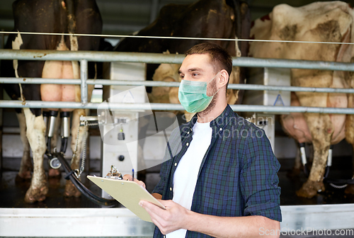 Image of man in mask with clipboard and cows on dairy farm