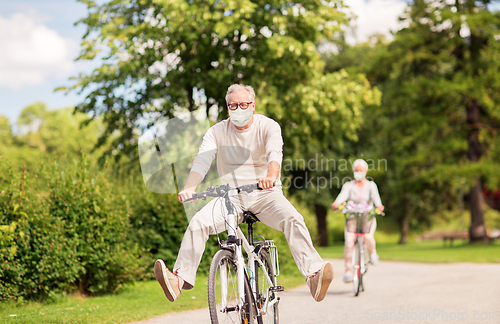 Image of senior couple in masks riding bicycles at park