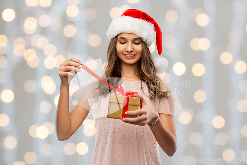 Image of teenage girl in santa hat opening christmas gift