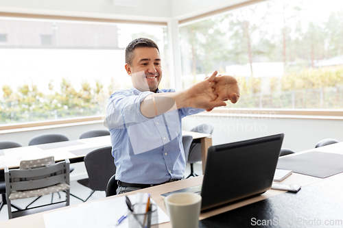 Image of tired man with laptop stretching at home office