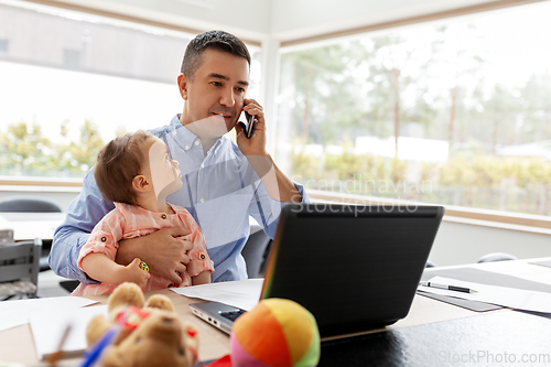 Image of father with baby calling on phone at home office