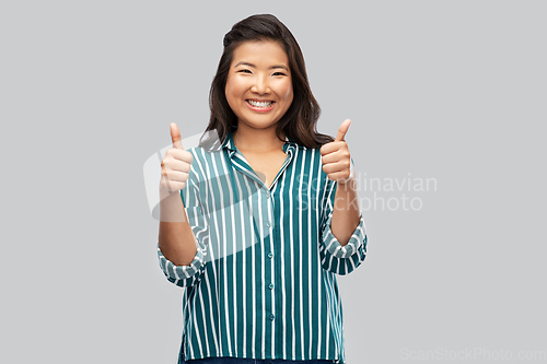 Image of happy asian woman showing thumbs up over grey