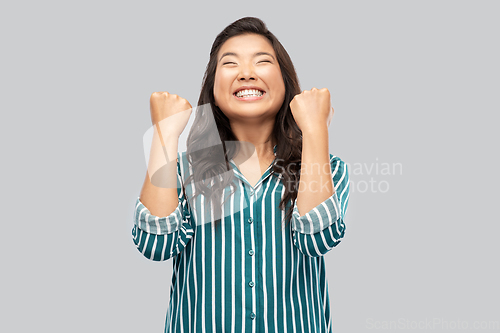 Image of happy asian woman celebrating success over grey