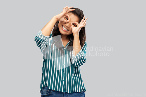 Image of smiling asian woman looking through finger glasses