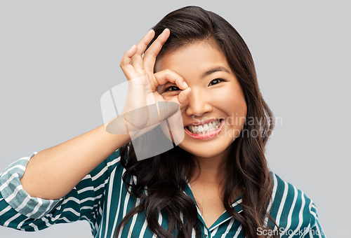 Image of smiling asian woman looking through finger glasses