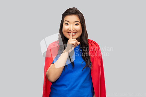 Image of asian woman in superhero cape making hush gesture