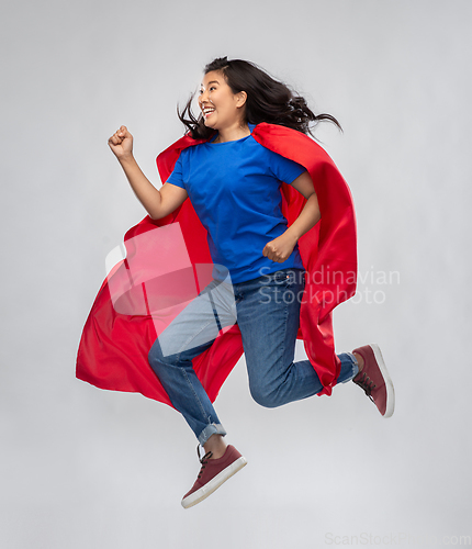 Image of happy asian woman in red superhero cape jumping