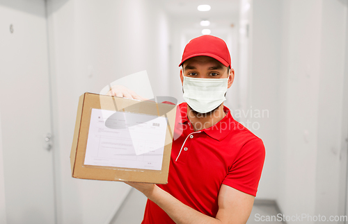 Image of delivery man in mask with parcel box in corridor