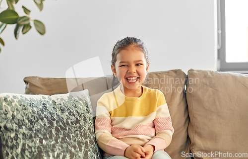 Image of happy smiling little girl sitting on sofa at home